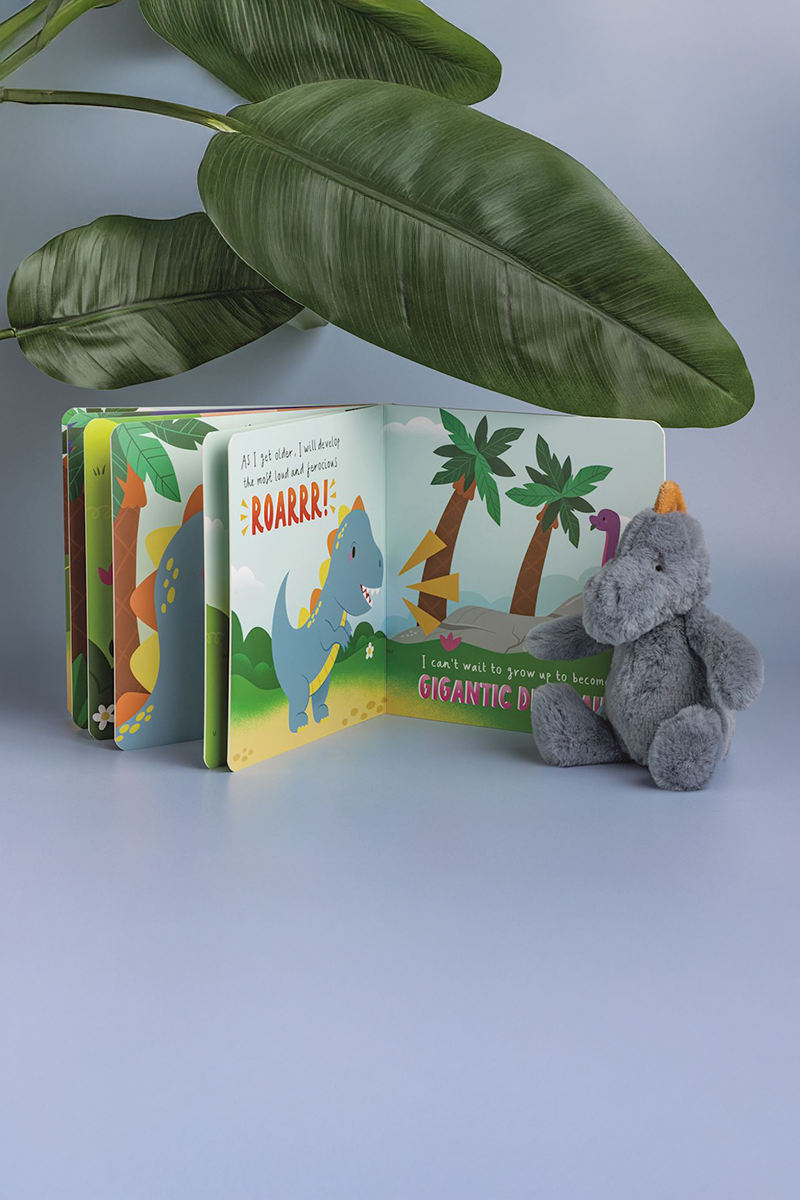 Children's book with dinosaur illustrations and a plush toy on a light gray background