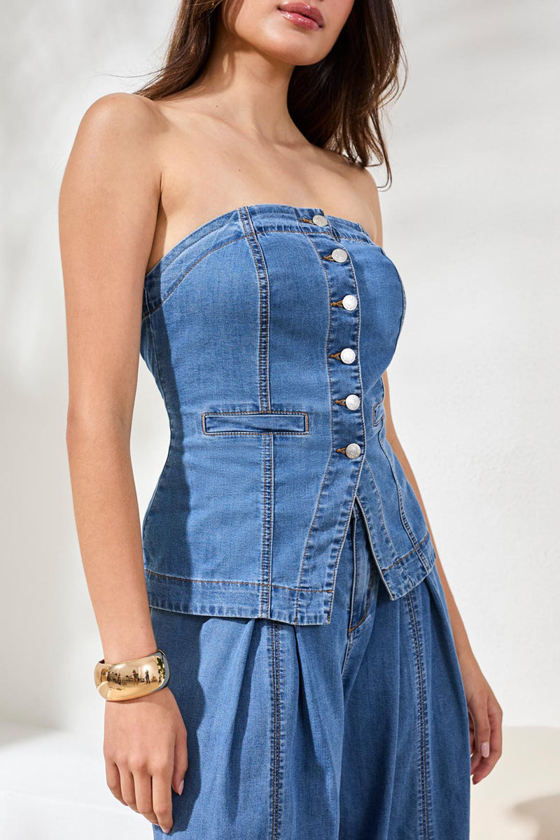 Woman wearing a blue denim strapless top with button details on a white background