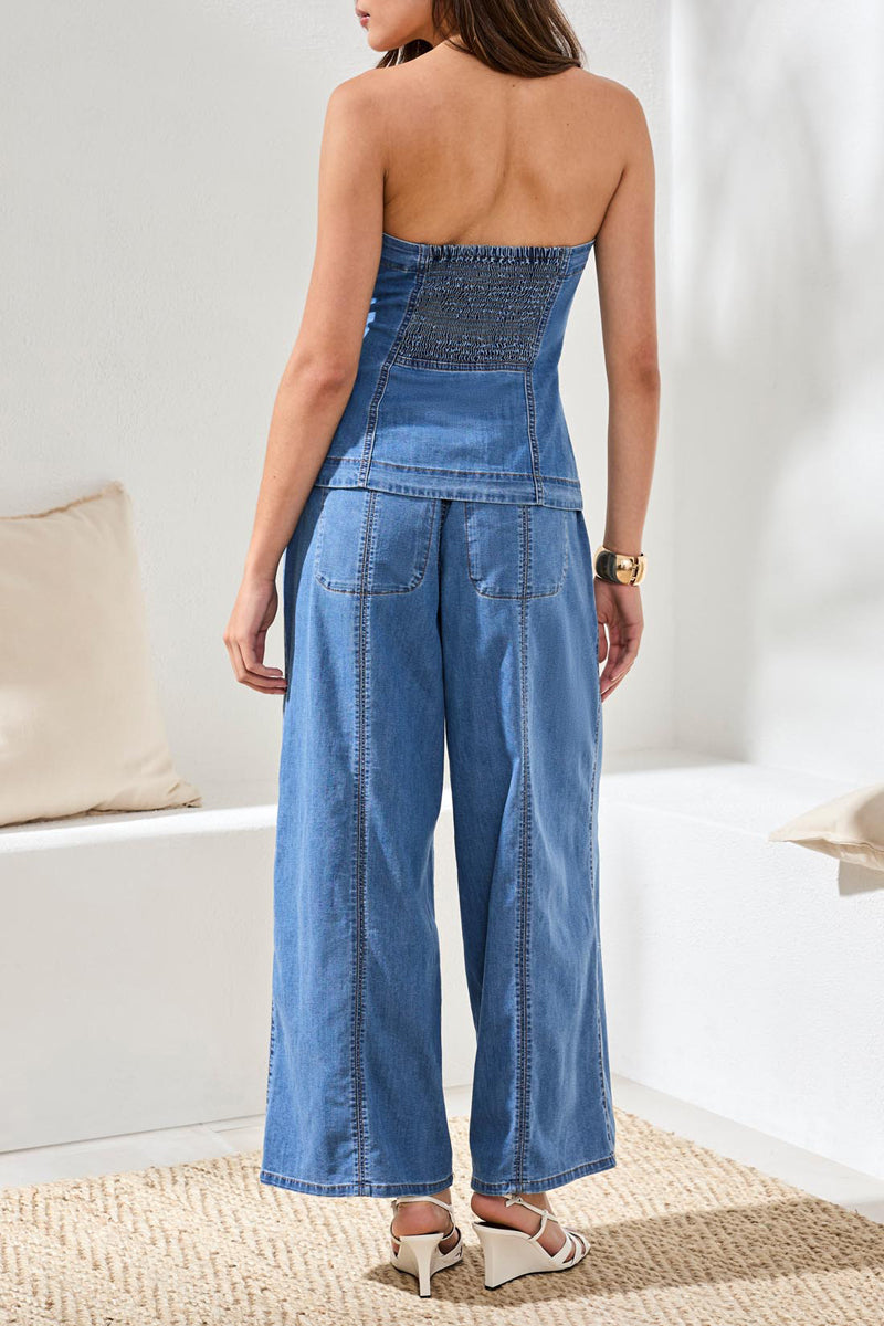 Woman wearing a blue denim strapless top and pants in a minimal indoor setting.