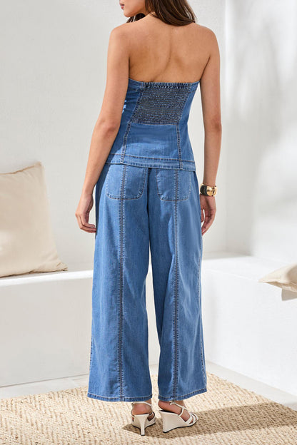 Woman wearing a blue denim strapless top and pants in a minimal indoor setting.
