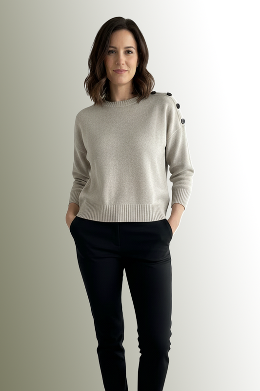 Woman wearing a light gray sweater with black buttons on a plain background