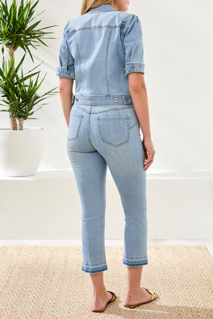 Person wearing a light blue denim jacket and jeans standing in a minimalistic room with a plant.