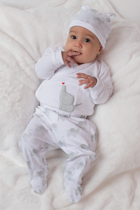 Baby in a white outfit with gray elephant design lying on a white blanket