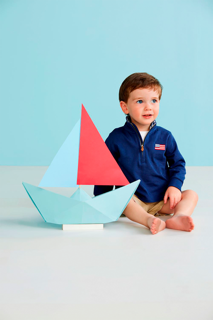 Child sitting next to a colorful paper boat on a light blue background