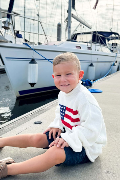 Child sitting on a dock with a boat in the background