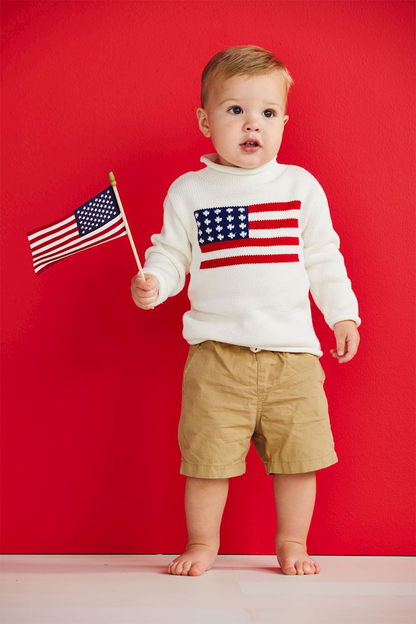 Little boy wearing white American flag sweater with shorts holding a flag on a red background