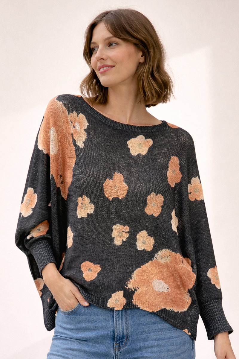 Woman wearing a black sweater with orangey brown floral patterns on a plain background