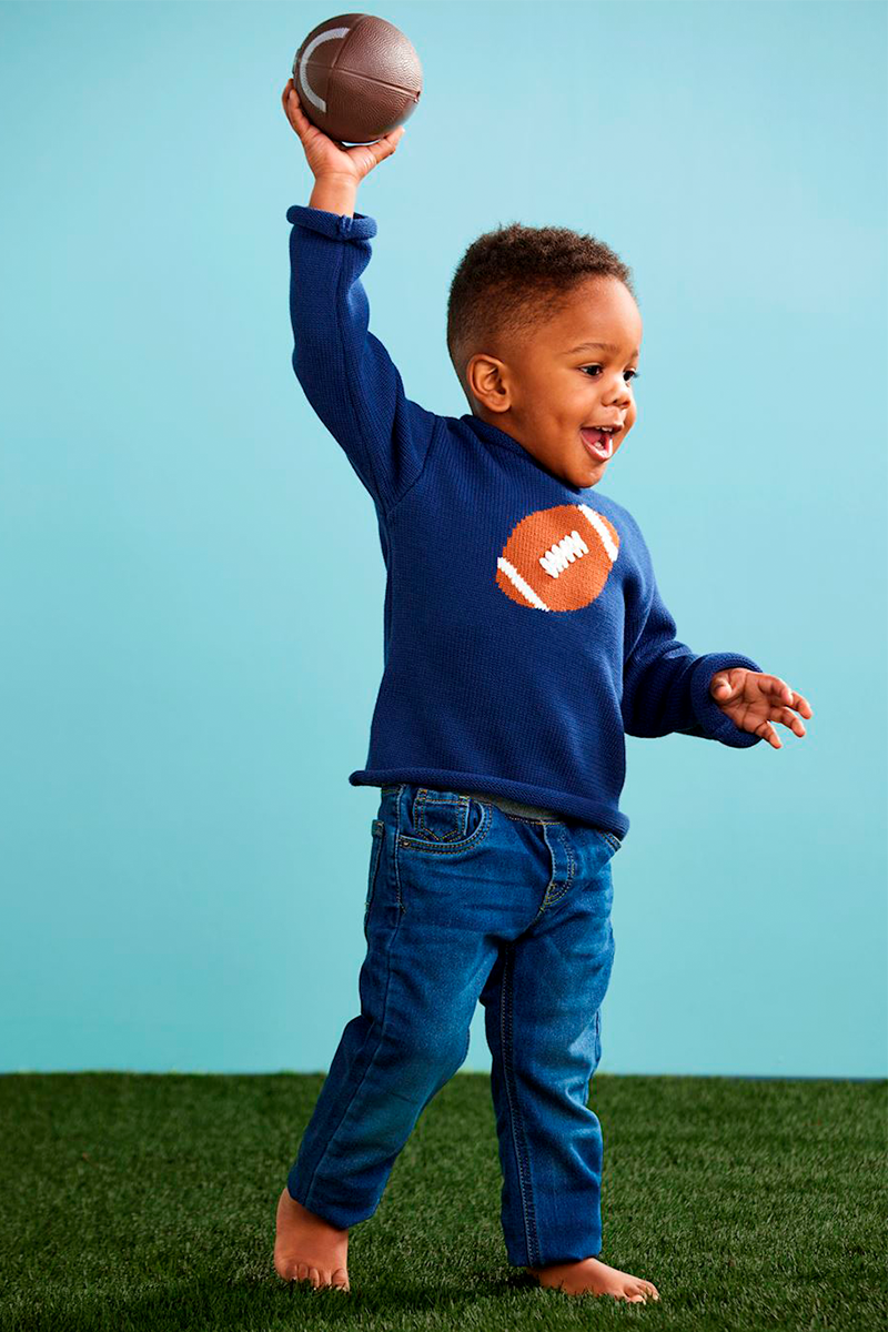 Child wearing a blue sweatshirt with a football design, holding a football against a light blue background.