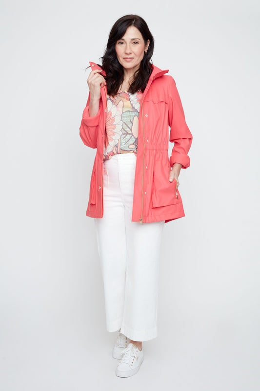 Woman wearing a coral raincoat over a patterned top and white pants on a white background