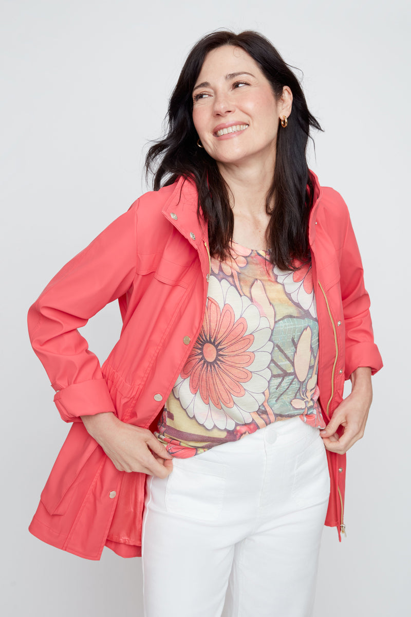 Woman wearing a coral jacket over a floral top and white pants on a light gray background