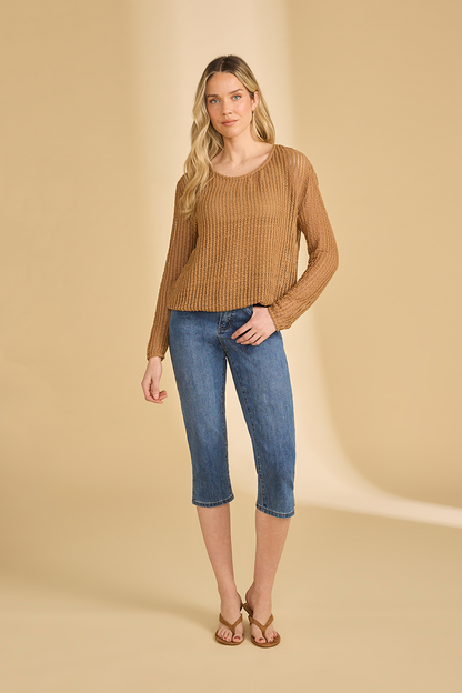 Woman wearing a brown open knit sweater and blue jeans on a beige background