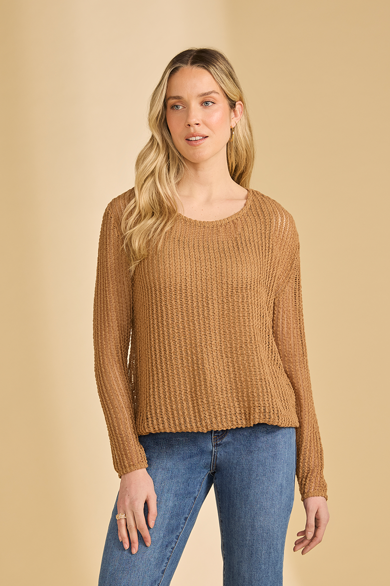 Woman wearing a brown open knit sweater and blue jeans against a beige background