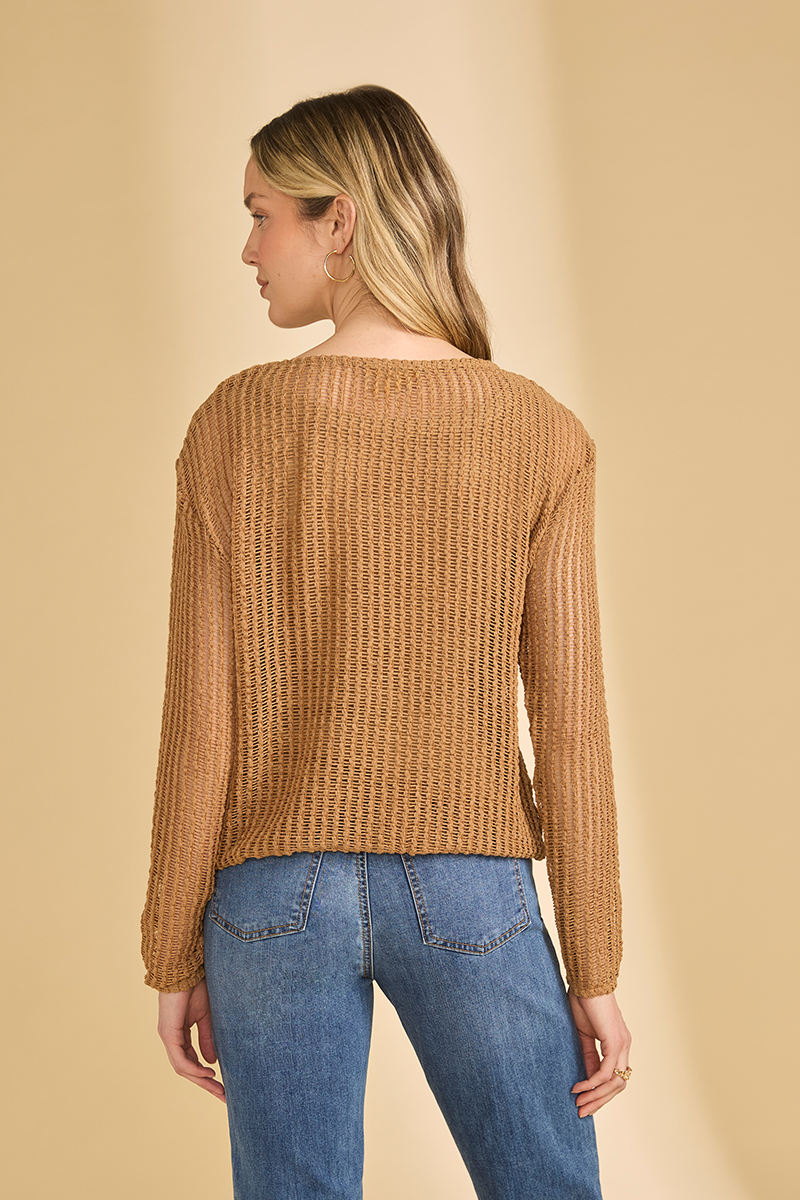 Woman wearing a brown open knit sweater and blue jeans on a beige background