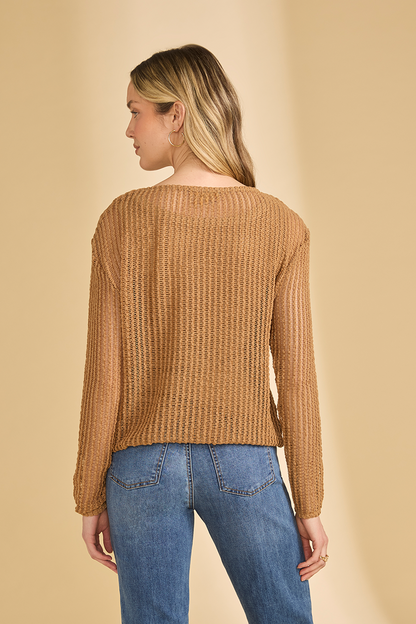 Woman wearing a brown open knit sweater and blue jeans on a beige background