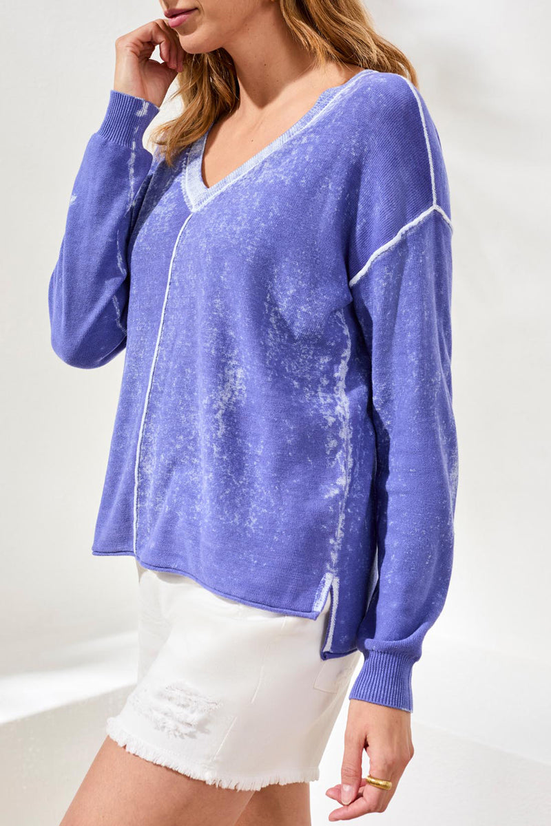 Woman wearing a blue distressed sweater with white shorts on a plain background