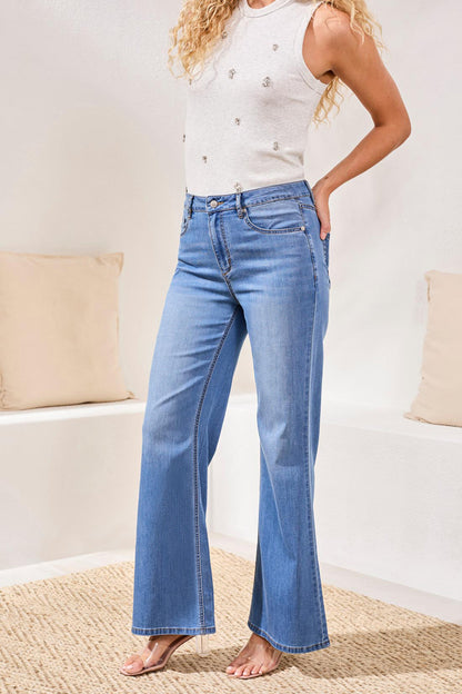 Person wearing blue jeans and a white sleeveless top in a casual setting.