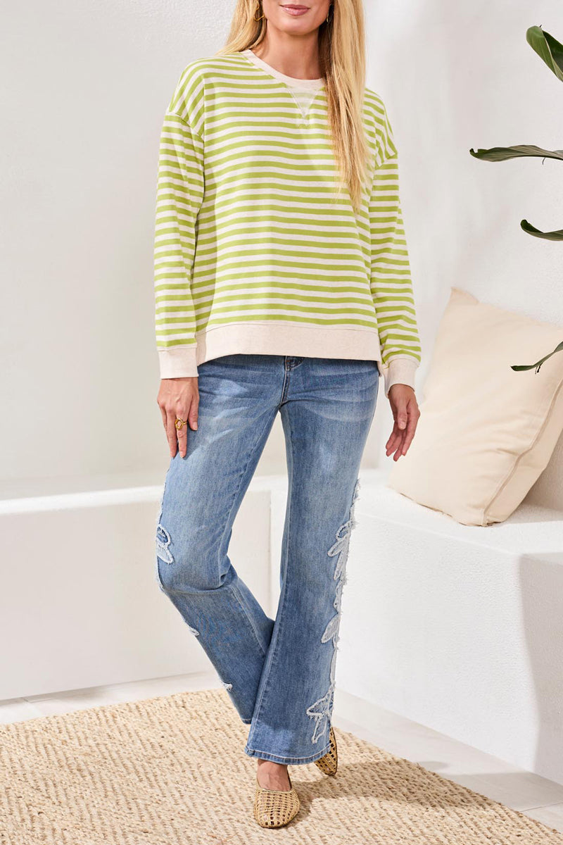 Woman wearing a green and white striped sweater and blue jeans indoors.