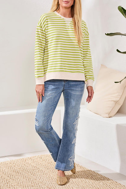 Woman wearing a green and white striped sweater and blue jeans indoors.