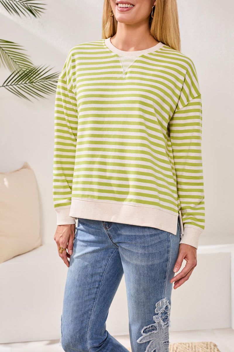 Woman wearing a green and white striped sweater and blue jeans indoors.
