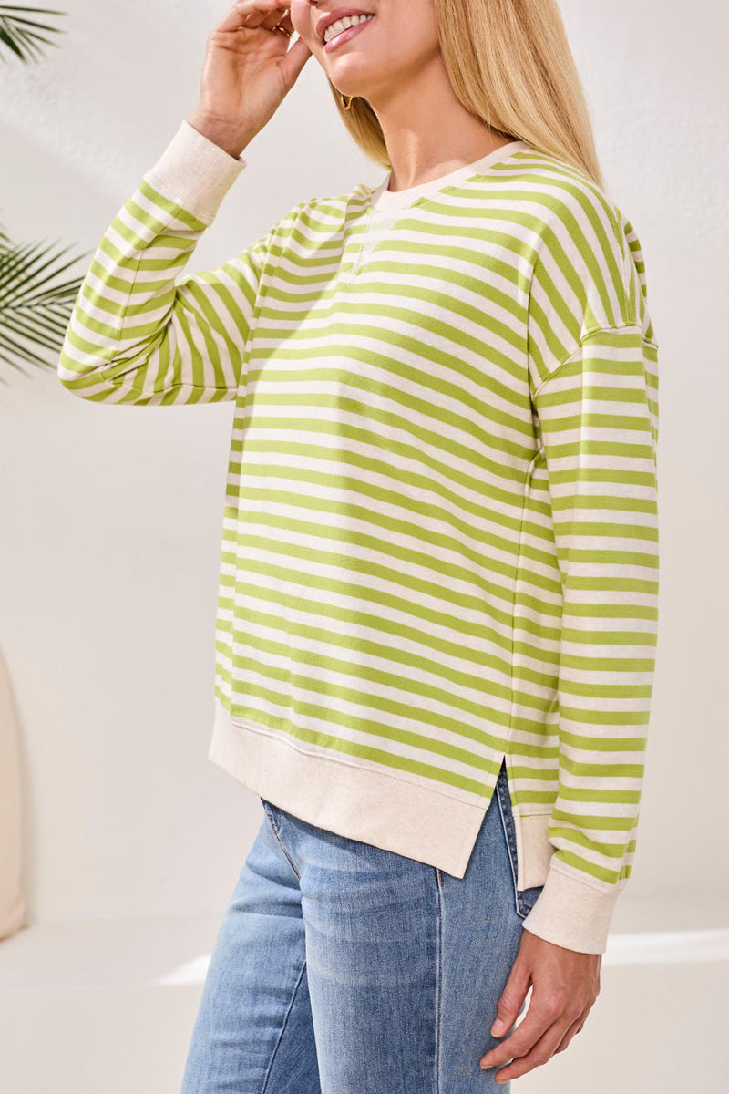 Woman wearing a green and white striped sweater with blue jeans against a neutral background