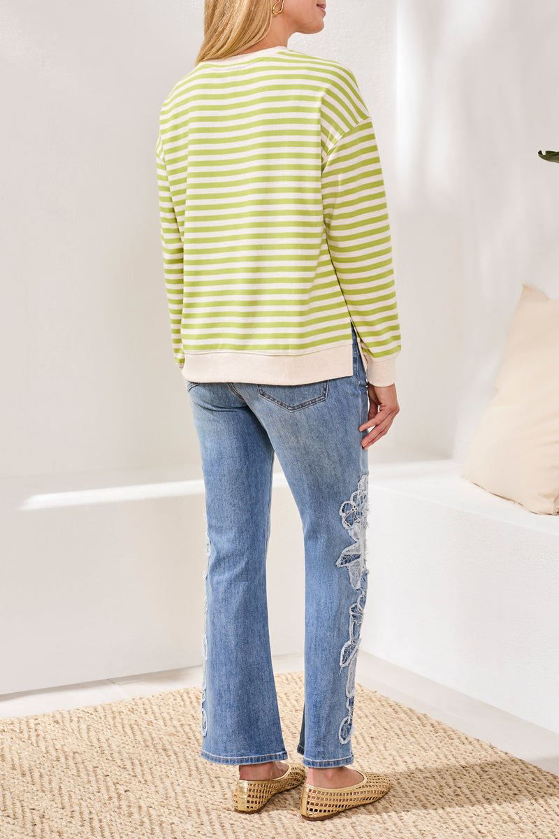 Woman wearing a green and white striped sweater and blue jeans in a room with a white wall and beige rug.