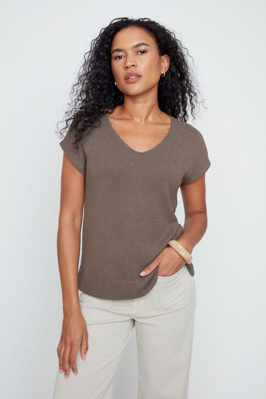 Woman wearing a brown t-shirt and white pants against a plain background