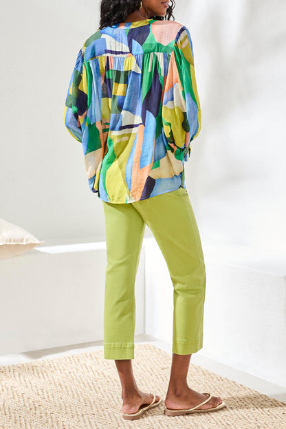 Person wearing a colorful patterned top and bright green pants on a white background
