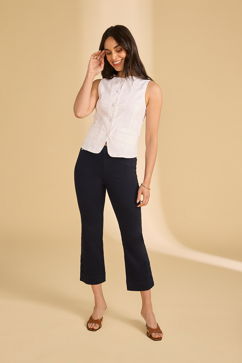 Woman wearing a white sleeveless blouse and black pants on a beige background