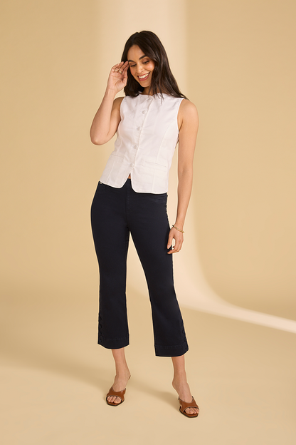 Woman wearing a white sleeveless blouse and black pants on a beige background