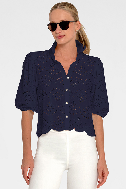 Woman wearing a navy blue eyelet button-up shirt with white pants on a plain background