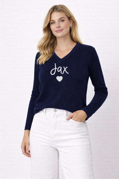 Woman wearing a navy sweater with 'jax' and a heart design on a white background