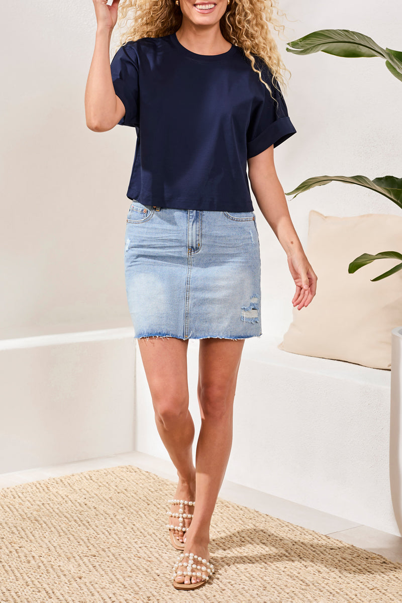 Woman wearing a navy top and light blue denim skirt indoors.