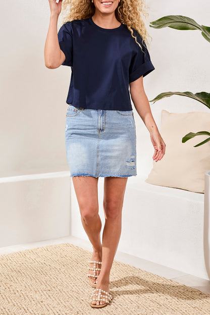 Woman wearing a navy top and light blue denim skirt indoors.
