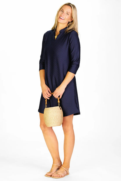 Woman wearing a navy dress holding a straw bag on a white background