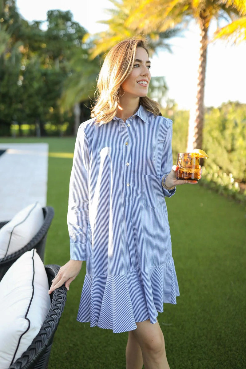 Woman in a blue and white striped dress holding a drink outdoors with palm trees in the background