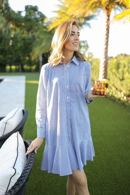 Woman in a blue and white striped dress holding a drink outdoors with palm trees in the background