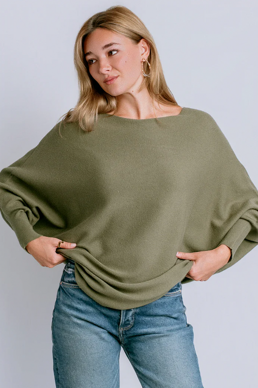 Woman wearing an olive green sweater and blue jeans against a plain background
