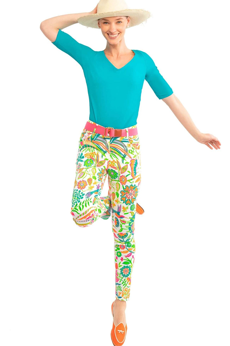 Woman wearing a turquoise top, pink belt, and colorful floral pants on a white background