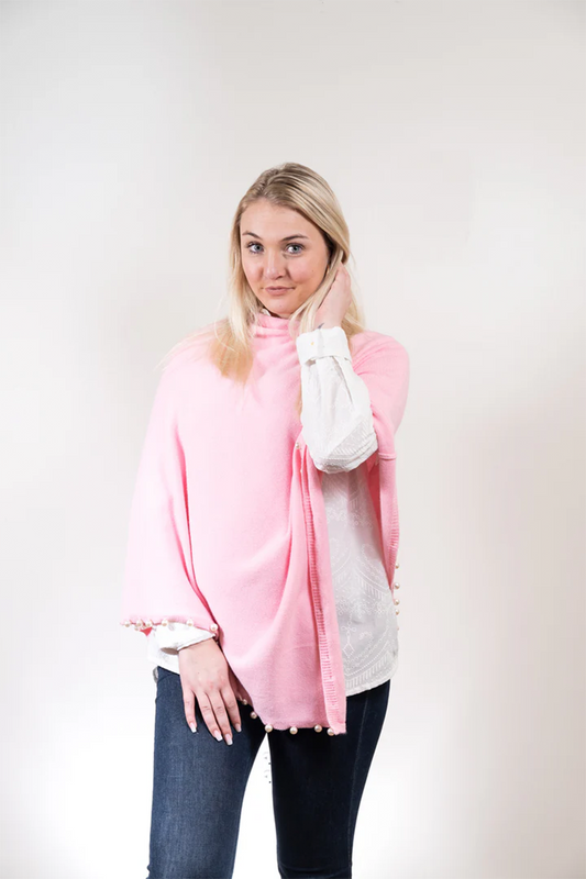 Woman wearing a pink poncho with pearl trim over a white shirt on a plain background