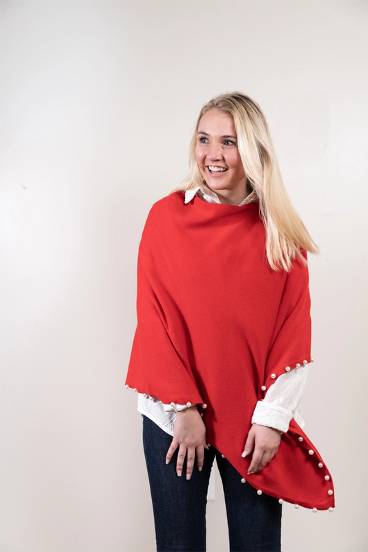 Woman wearing a red poncho with pearl trim against a plain background