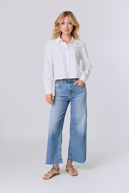 Woman wearing a white shirt with decorative rhinestone elements and blue jeans on a white background