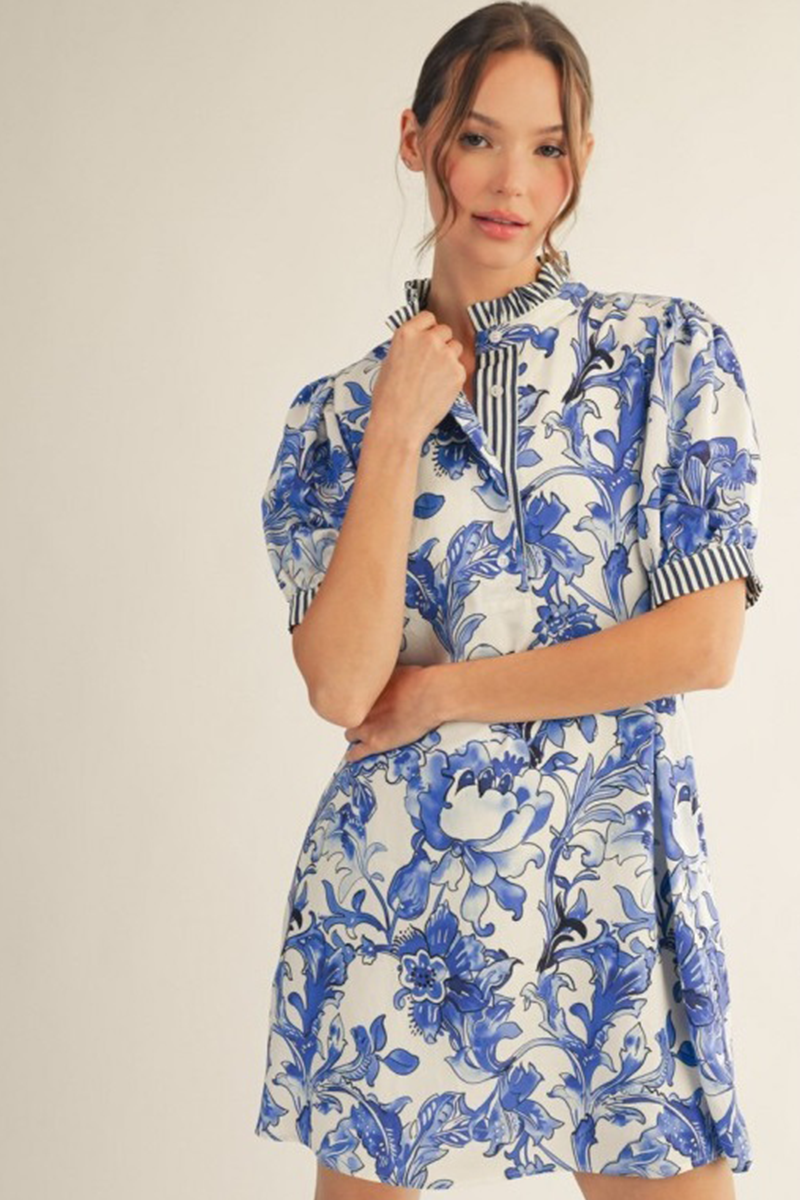 Woman wearing a blue and white floral dress with a striped shirt underneath on a plain background