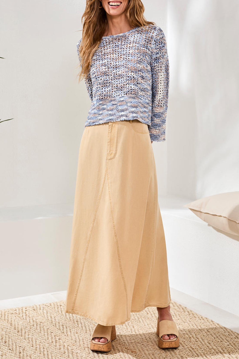 Woman wearing a patterned top and beige skirt in a minimal indoor setting