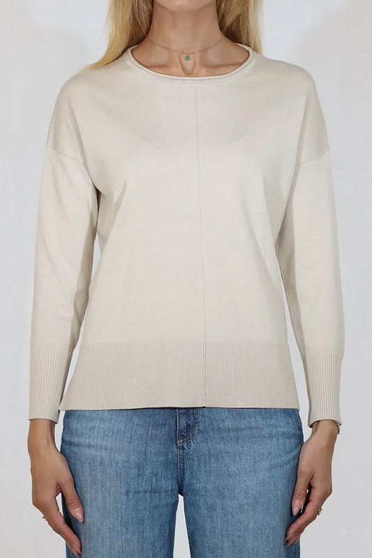 Woman wearing a beige sweater and blue jeans against a white background