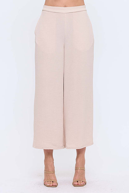 Woman wearing neutral wide leg pants with nude heels on white background