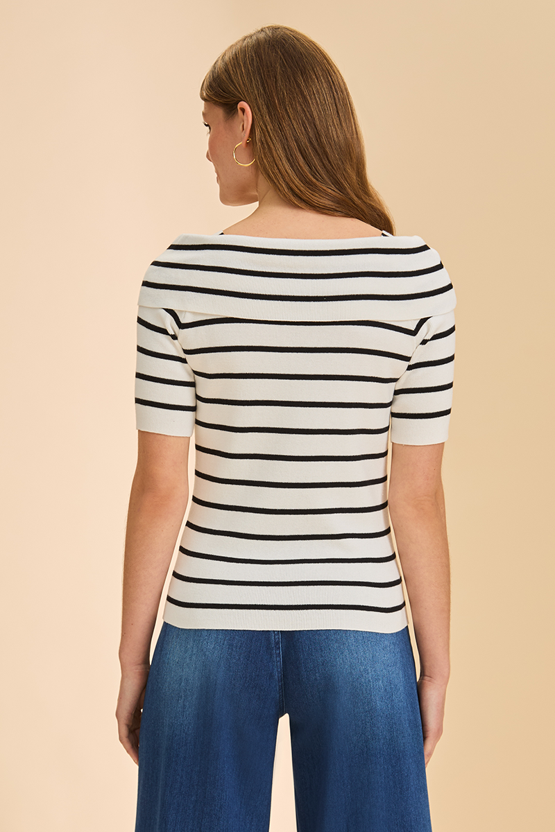 Woman wearing a black and white striped shirt with blue pants on a beige background