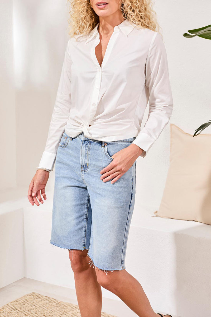 Woman wearing a white shirt and light blue denim shorts in a minimalistic room.