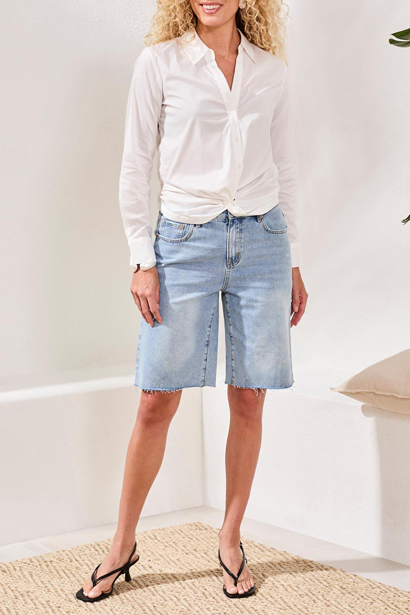 Woman wearing a white shirt and light blue denim shorts indoors.