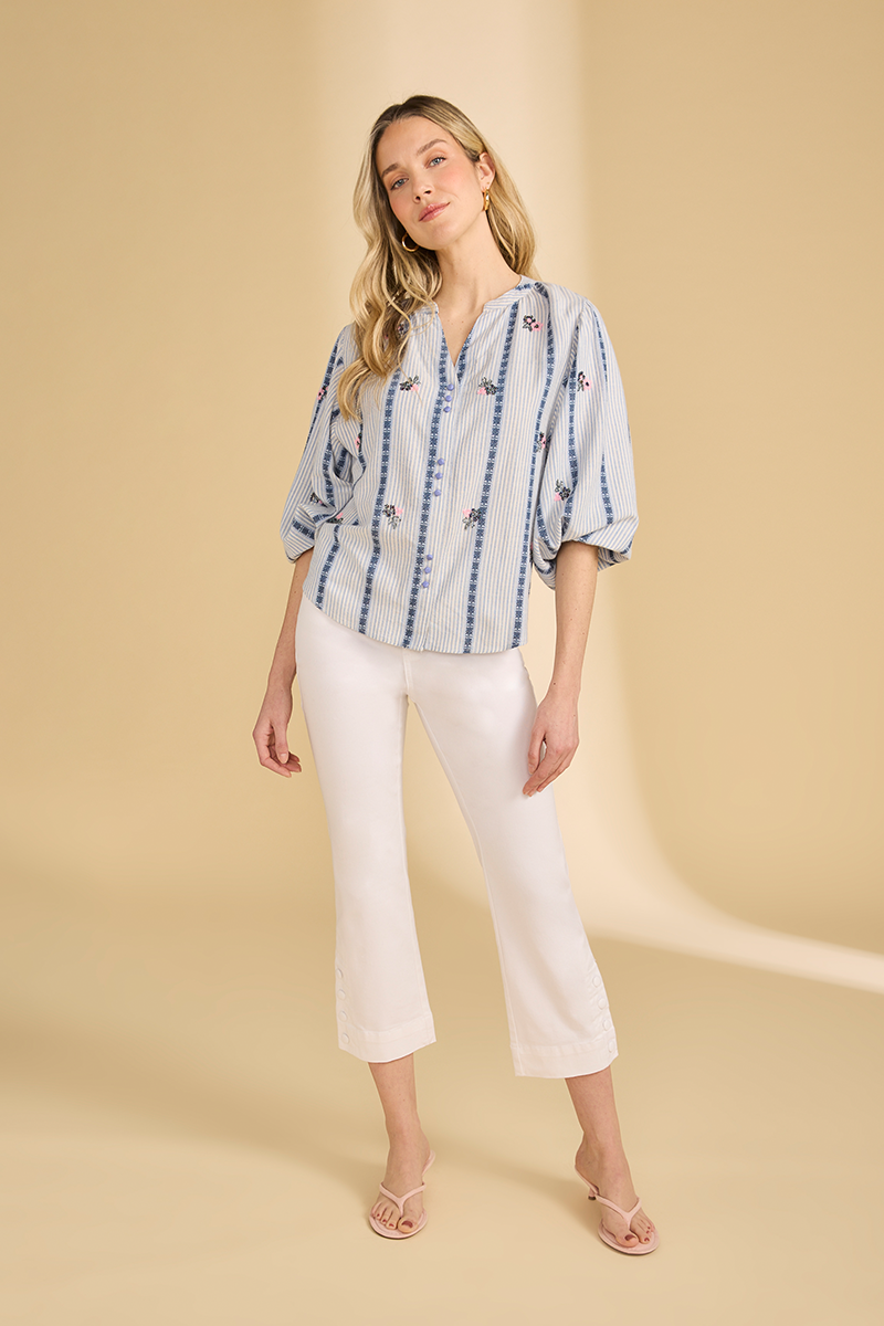 Woman wearing a blue and white striped blouse with white pants on a beige background