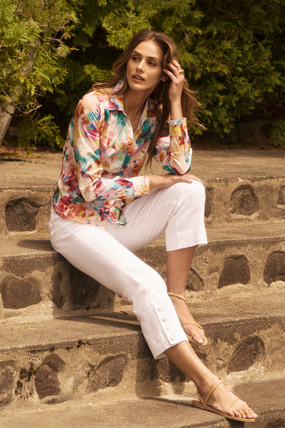 Woman sitting on stone steps wearing a colorful floral blouse and white pants.